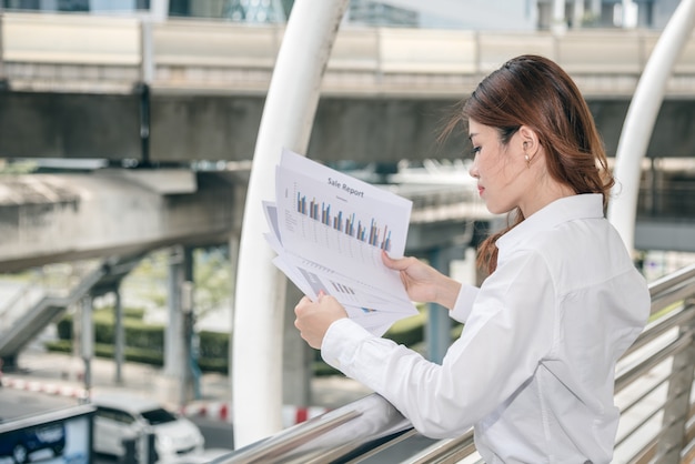 Portretten van mooie Aziatische vrouw in denkende uitdrukking die met financieel grafiekdocument werken