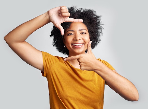 Portretvingerframe en gelukkige vrouw in witte achtergrondstudio en beoordeling profielfoto Gezicht jong vrouwelijk model en handen om perspectief coole selfie te begrenzen en glimlachen voor creatieve fotografie