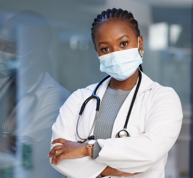Portretvirus en armen gekruist met een dokter zwarte vrouw in het ziekenhuis met een masker op voor de veiligheid Medische gezondheidszorg en verzekering met een vrouwelijke arts die u kunt vertrouwen in een kliniek