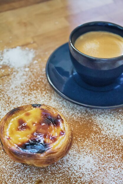 Portuguese egg tart with a black cup of coffee behind