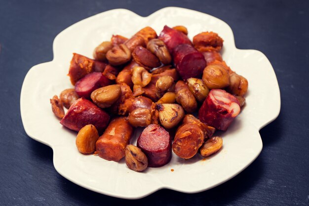 Salsiccie affumicate portoghesi con le castagne sul piatto bianco