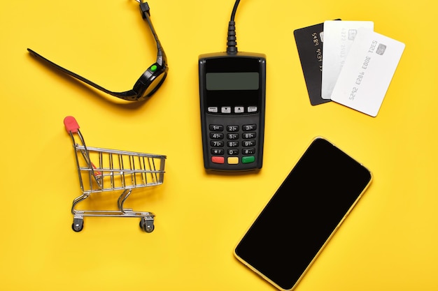 Платежный терминал POS смотрит банковские карты и смартфон на желтом Минимальная концепция финансовых услуг Модные тени копируют пространство