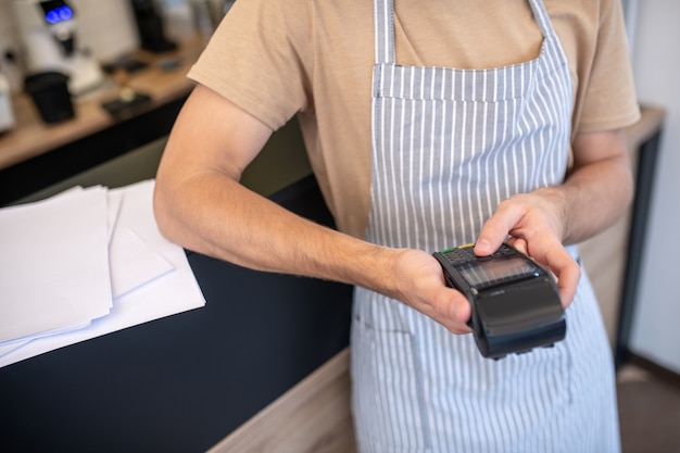 Pos-terminal voor cafés. Mannelijke handen met zwarte handige pos-terminal kiezen drukknop erop in café, geen gezicht