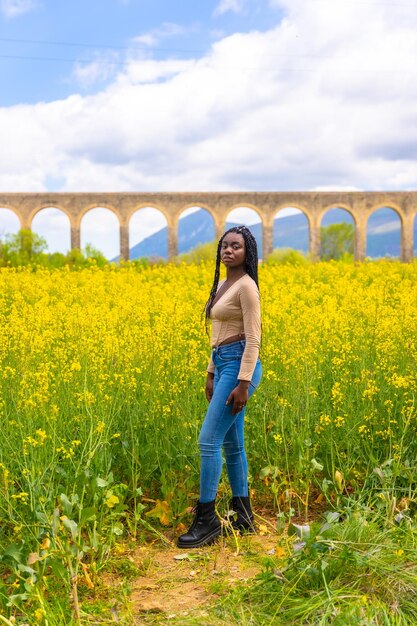 Posed smiling black ethnic girl with braids traveler in a field of yellow flowers