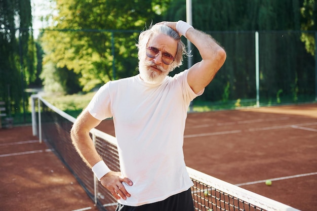 Poseren voor een camera In zonnebril Senior moderne stijlvolle man buiten op het sportieve veld overdag