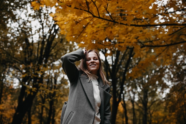 Poseren voor een fotoshoot in de natuur herfstportret van een jong meisje in een herfstpark in een grijze jas