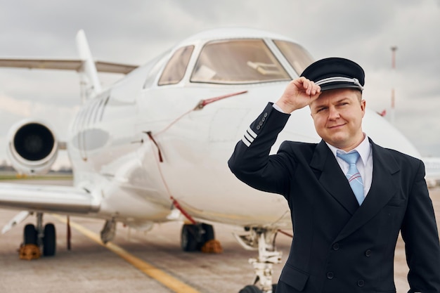 Posing for a camera Experienced pilot in uniform standing outside near plane