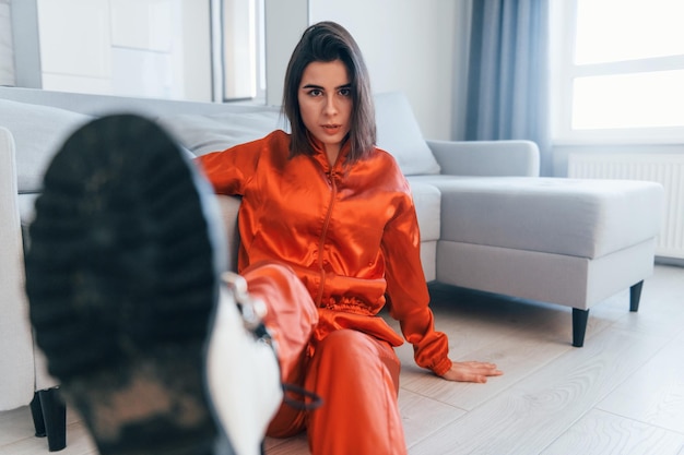 Posing for a camera in red costume Young woman is indoors in room of modern house at daytime