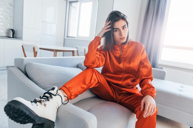 Posing for a camera in red costume Young woman is indoors in room of modern house at daytime