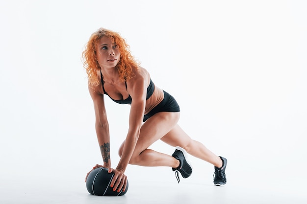 Posing for a camera with soccer ball. Particle view. Redhead female bodybuilder is in the studio on white space.