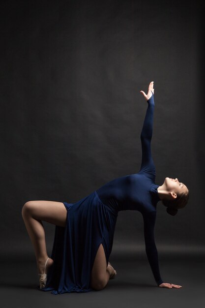 Posing dancer in long deep blue dress over dark background