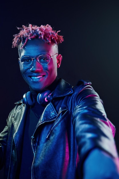 Posing with wireless headphones on neck Futuristic neon lighting Young african american man in the studio