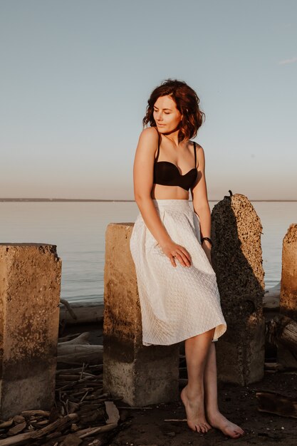 Posing woman in nature. Young woman in stylish clothes:  top and white skirt  sitting  on stones  against the backdrop of a  sea.