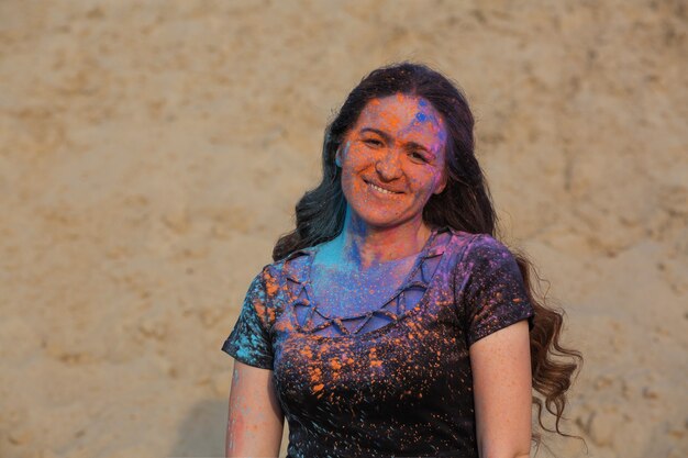 Positief brunette meisje met lang krullend haar bedekt met kleurrijk droog poeder Holi in de woestijn. Ruimte voor tekst