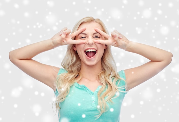 positief gebaar, emotie, wintervakanties, kerstmis en mensenconcept - glimlachende jonge vrouw of tienermeisje die vrede toont handteken met beide handen over sneeuw