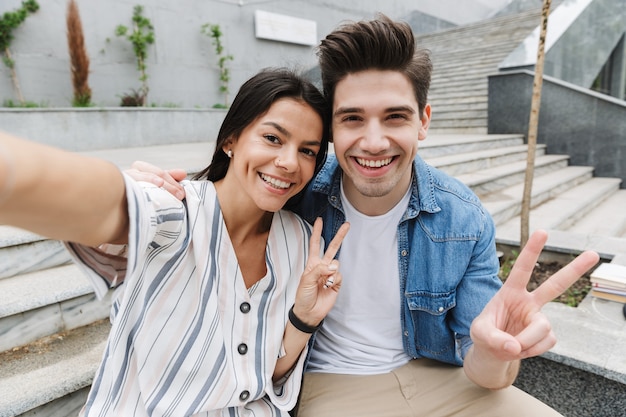 positief glimlachend vrolijk jong stel buiten neemt een selfie door de camera die vrede toont.