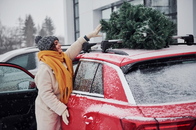 Positief jong meisje dat in de buurt van de auto staat met een groene kerstboom erop