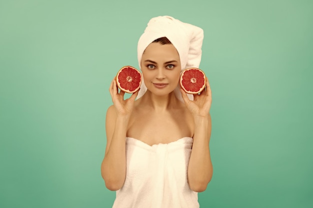 Positief jong meisje in handdoek na douche met grapefruit op blauwe achtergrond