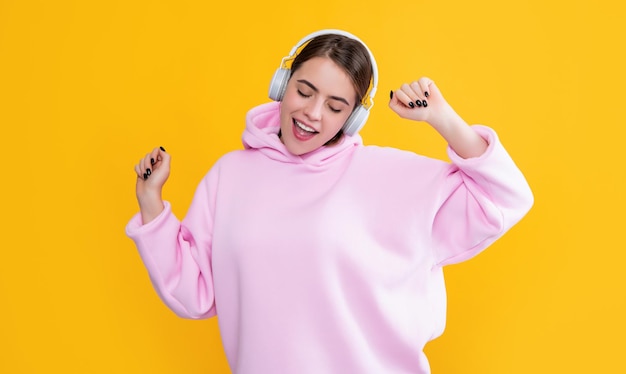 Positief jong meisje luistert muziek in koptelefoon op gele achtergrond