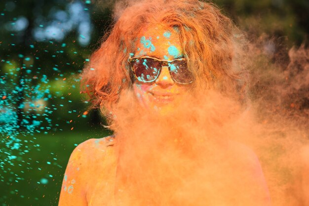 Positief jong model dat plezier heeft in een wolk van oranje droog poeder en het Holi-kleurenfestival viert