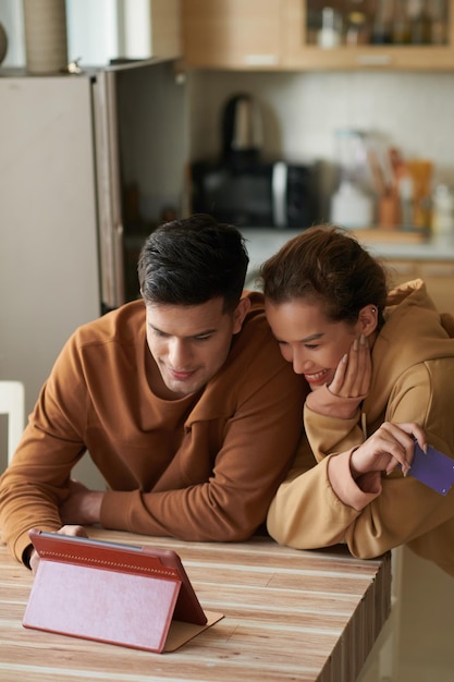 Positief jong stel dat online winkel op tabletcomputer controleert en kiest wat te bestellen voor het avondeten