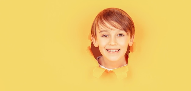 Positief kind met brede, aangename glimlach op gezicht blijft door gescheurd gat in blu-papier Kid met brede glimlach toont gezicht in papiergat