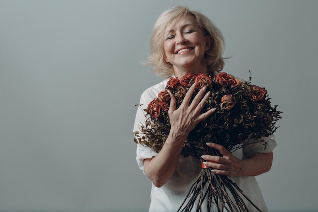 Positief lachende oudere vrouw in handen roze bloemenboeket houden