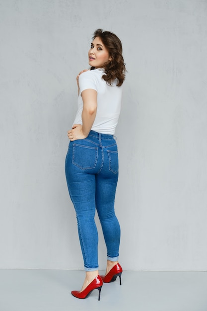 Positief meisje in jeans, wit t-shirt en rode stiletto's poseren