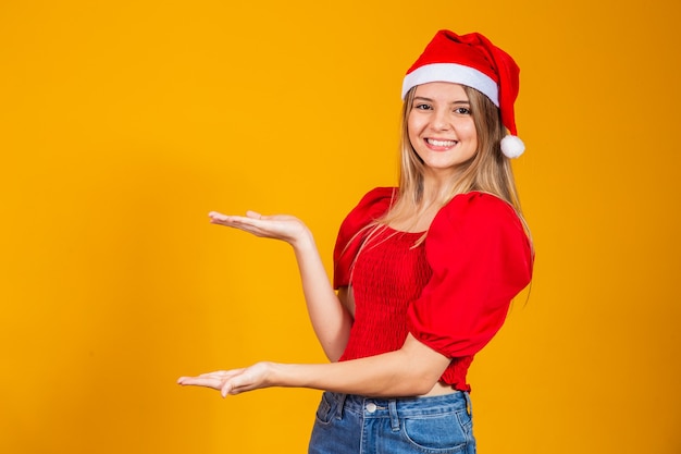 Positief meisje in kerstmuts wijzend op tekstruimte. promotie en advertenties geïsoleerd op gele achtergrond.