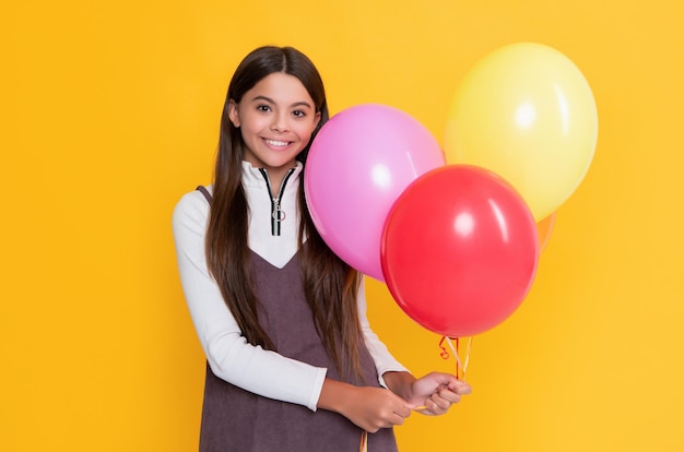 Positief meisje met partij kleurrijke ballonnen op gele achtergrond