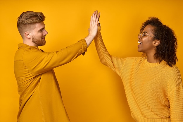 Positief multicultureel stel geeft high five en stemt ermee in om te werken terwijl het team zijwaarts op de gele muur staat