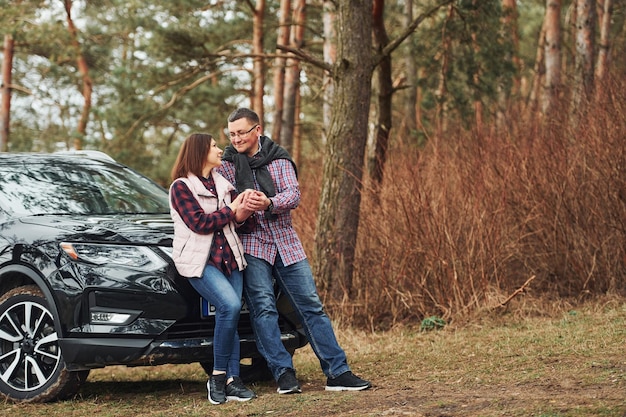 Positief volwassen stel dat in de buurt van hun auto staat met een warm drankje in handen Buiten in het bos