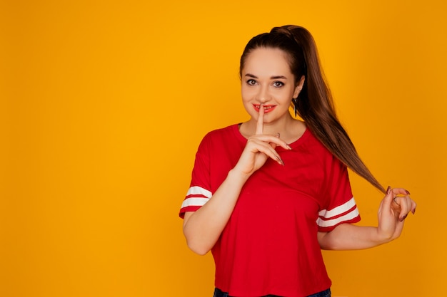 Positief vrolijk meisje dat een rode t-shirt op gele achtergrond draagt