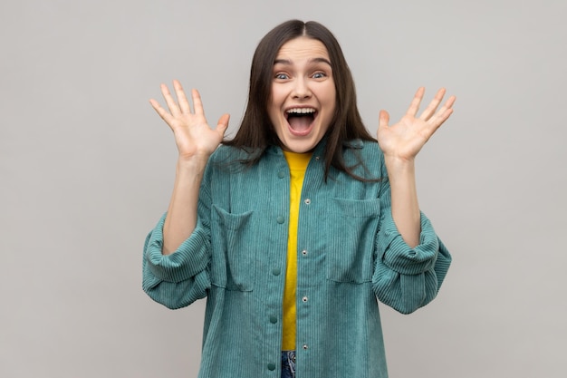 Positieve aantrekkelijke vrouw die met opwinding naar de camera kijkt, hief haar armen aangename verrassing op