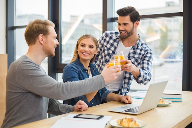 Positieve aardige jonge mensen die samen staan en juichen met sap terwijl ze hun succes vieren