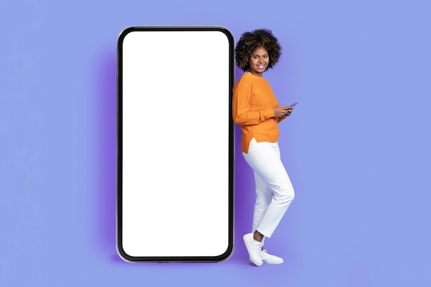 Positieve afro-amerikaanse dame leunend op een enorm telefoonmodel