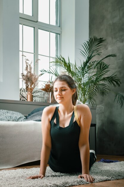 Positieve atletische vrouw met netjes gebonden haar en strakke sportkleding die zich thuis uitrekt.