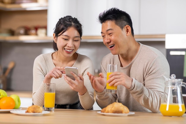Positieve Aziatische familie die smartphone gebruikt terwijl ze thuis ontbijten