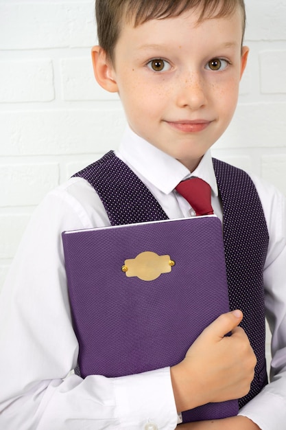 Positieve basisschoolnerdstudent die een leerboek vasthoudt en naar jou kijkt op een lichte achtergrond