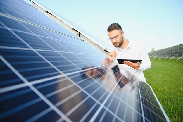 Positieve bebaarde mannelijke investeerder die tegen fotovoltaïsche panelen staat die alternatieve energie produceren