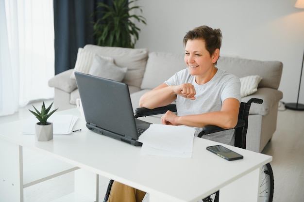 Positieve bejaarde vrouw in rolstoel die online aan laptop IT freelancer werkt