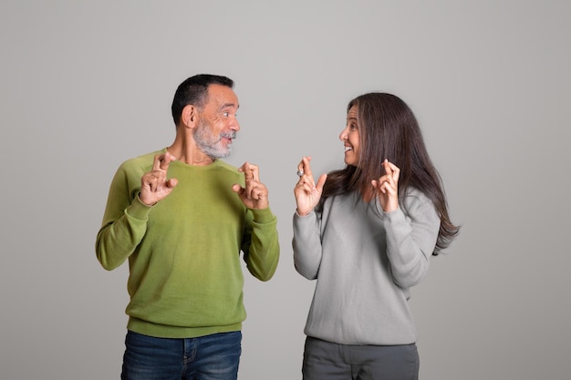 Positieve blanke oude man en vrouw gekruiste vingers dromen van overwinning en doen een wens