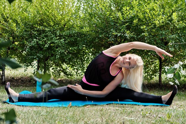 Positieve blonde vrouw voert rekoefeningen uit in het park. Fitness buitentraining