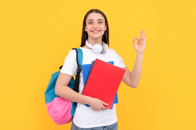 Positieve dame in koptelefoon houdt voorbeeldenboek vast en draagt rugzak terug naar school