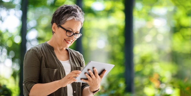 Positieve dame van middelbare leeftijd die online nieuws op een digitale tablet leest