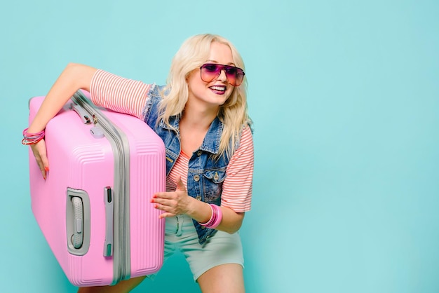 Positieve emotie vrouw met zak roze koffer op gekleurde achtergrond. Reisconcept.