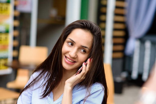 Positieve emoties lifestyle concept close up van jonge charmante donkerharige blanke vrouw in zwarte jurk glimlachend met tanden opzij kijken met ontspannen uitdrukking chatten met vriendje op telefoon