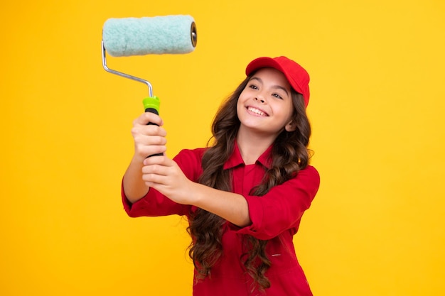 Positieve en lachende bouwer in het bouwen van uniform en pet Schilder schilderen met verfroller Werknemer geïsoleerd op gele achtergrond Kids renovatie concept