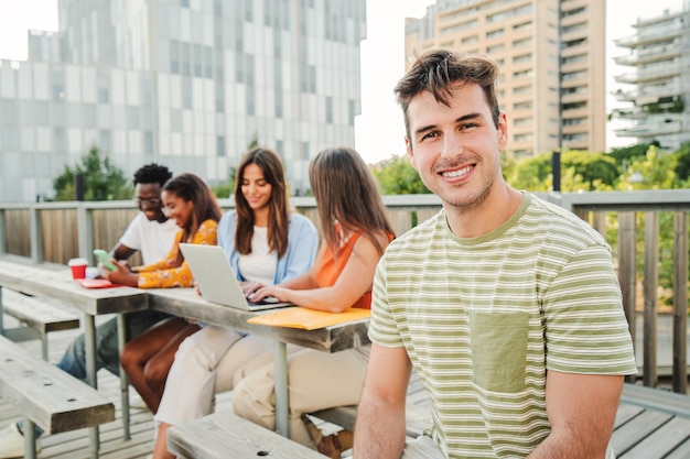 Positieve en lachende jonge student die naar de camera kijkt terwijl hij met een vriend zit op de universiteitscampus