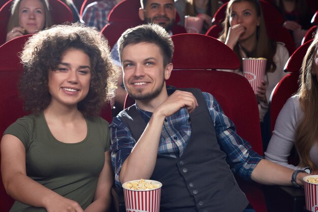 Positieve en stijlvolle vriend en vriendin kijken naar film in de bioscoop